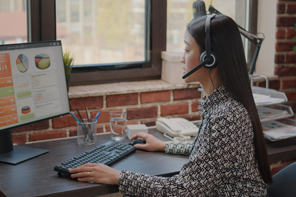 TP CRCD - Jeune femme assise à un bureau en train de travailler sur un ordinateur, un casque micro sur la tête